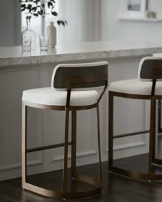 two white stools sitting next to each other on a wooden floor in front of a counter