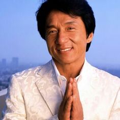 a man in a white suit smiling and holding his hands together