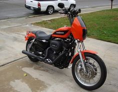 an orange motorcycle parked on the sidewalk next to some cars