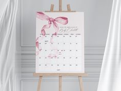 an easel with a calendar on it in front of a white wall and curtains