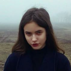 a young woman standing in the middle of a field on a foggy day, looking at the camera