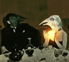 two people sitting at a table with masks on their faces and one person holding a lit candle in front of them