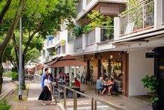 people are sitting at tables on the side walk in front of an apartment building with balconies