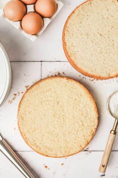 two cakes on a table with eggs and measuring spoons next to the top one