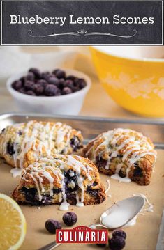 blueberry scones on a baking sheet with lemon wedges and bowl of berries in the background