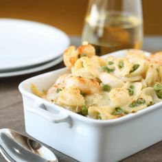 a white dish filled with pasta and shrimp next to a glass of wine on a table