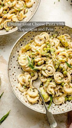 two bowls filled with pasta and vegetables on top of a white table next to utensils