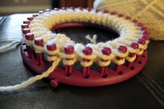 a red and white object sitting on top of a table next to a ball of yarn