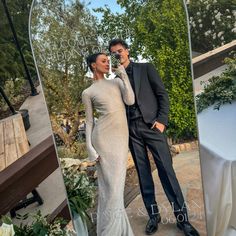 a man and woman standing next to each other in front of a mirror with flowers