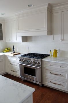 a kitchen with white cabinets and stainless steel stove top oven in the center, surrounded by wooden flooring