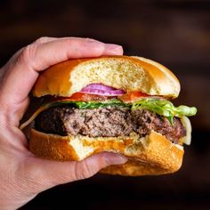 a hand holding a hamburger with meat, cheese and lettuce on it's bun