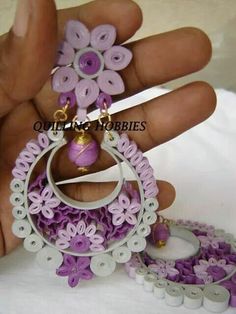 a hand is holding some purple and white beads with flowers on them, as if it were made out of paper