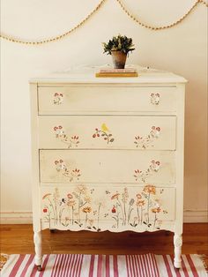 a white dresser with flowers painted on the front and drawers, next to a striped rug