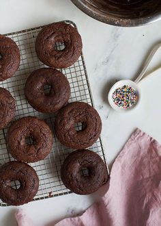 chocolate doughnuts on a cooling rack with sprinkles and a spoon