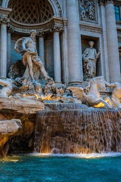 an image of a fountain in front of a building that has statues on it and water running down the side