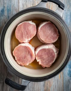 four raw pork chops in a pot on a wooden table