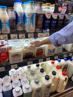 a person is picking up milk from a shelf in a grocery store with other items