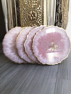 three pink plates sitting on top of a wooden floor next to a gold vase and mirror