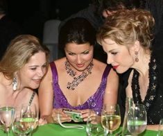 three women sitting at a table looking at a cell phone