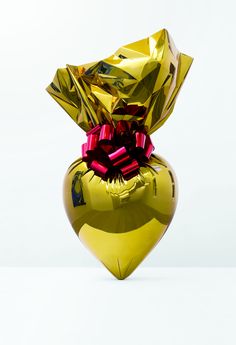 a shiny gold heart shaped vase with red bows