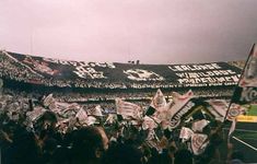 a stadium full of people holding flags and banners in front of the stands with an overcast sky