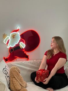 a woman sitting on a bed holding a red gift box in front of a santa clause sign