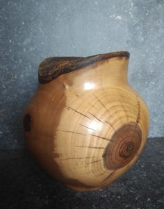 a wooden vase sitting on top of a black counter next to a gray stone wall