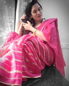 a woman in a pink and gold sari sitting down with her hair combed