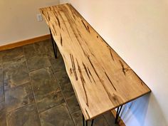 a wooden table sitting on top of a tile floor next to a white wall with black hairpin legs