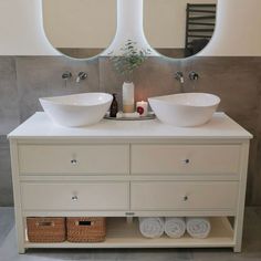 two white sinks sitting on top of a bathroom counter next to mirrors and baskets under them