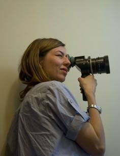 a woman holding a camera up to her face and looking into the distance with it's lens