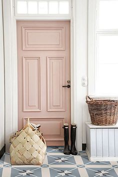 a pink door with a basket and boots on the floor next to it, in front of a white wall