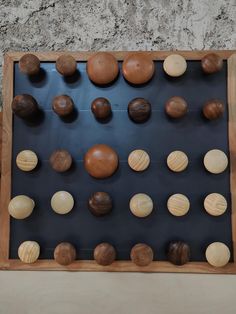 a wooden board with many different sized and shapes balls on the back side, in front of a stone wall