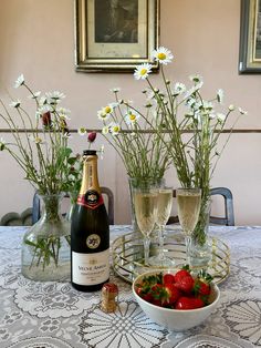 two wine glasses and some strawberries on a table with flowers in the vases