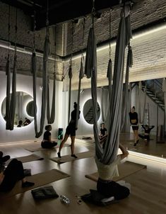 people doing yoga in a large room with mirrors on the wall and hanging hammocks