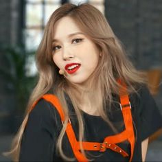 a woman with long blonde hair wearing an orange suspender and red lipstick is looking at the camera