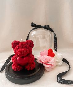 a red teddy bear sitting on top of a black plate next to a pink flower