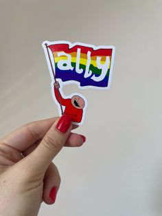 a person holding a sticker with the word july on it and a rainbow flag