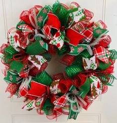 a red and green christmas wreath hanging on the front door with ribbon attached to it