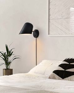 a bed with a black lamp next to it and a potted plant on the side