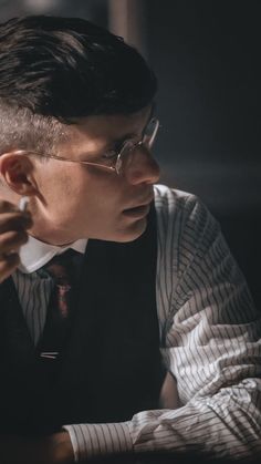 a man wearing glasses and a tie sitting at a table with his hand on his chin