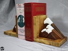 three books are stacked on top of each other in front of a bookend made out of wood