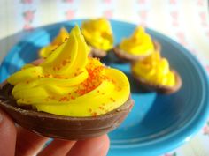 a hand holding a chocolate cupcake with yellow frosting and sprinkles