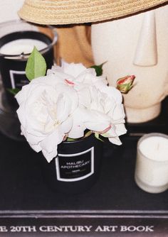 a white rose sits in a black vase next to two candles and a straw hat