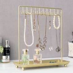 a gold jewelry holder with necklaces and perfume bottles on it next to other items