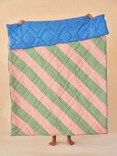 a person holding up a pink and green striped quilt