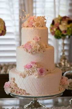 a wedding cake with pink flowers on the top and white icing, sitting on a table