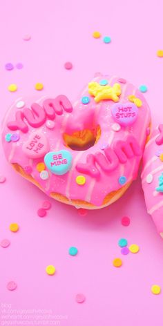 two donuts with pink frosting and sprinkles are on a pink surface