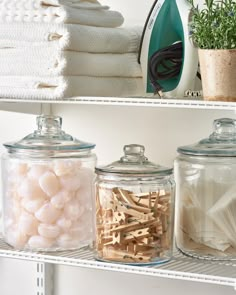 three glass jars filled with different types of items on top of a white shelf next to a potted plant