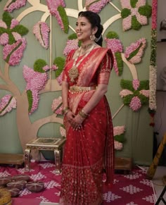 a woman in a red sari standing next to a wall with pink flowers on it